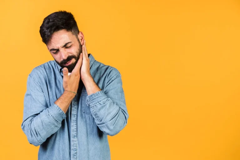 Man holding his jaw in pain against a yellow background, representing the urgency of dental emergencies and the need for immediate dental care.