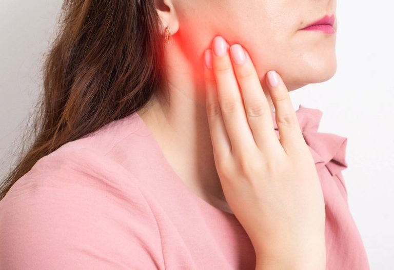 Woman experiencing dental pain, holding her jaw, indicating discomfort, with a focus on the affected area in the context of emergency dental care.