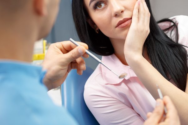 Woman in dental chair experiencing tooth pain, consulting with dentist holding dental instruments, emphasizing urgent dental care and treatment options.