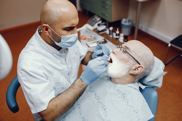 Dentist providing dental care to elderly patient in clinic, emphasizing emergency dental treatment and oral health restoration.